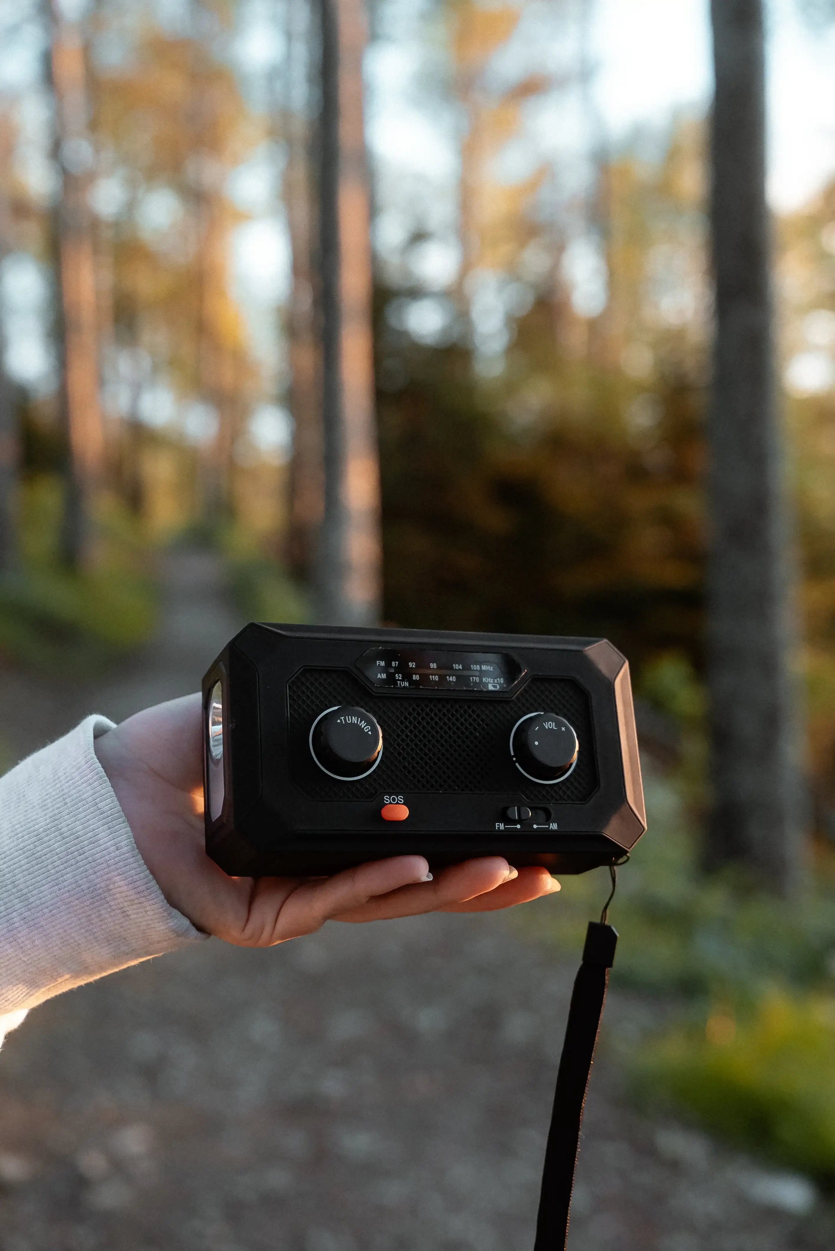 En person håller upp en svart vevradio med inbyggd ficklampa.