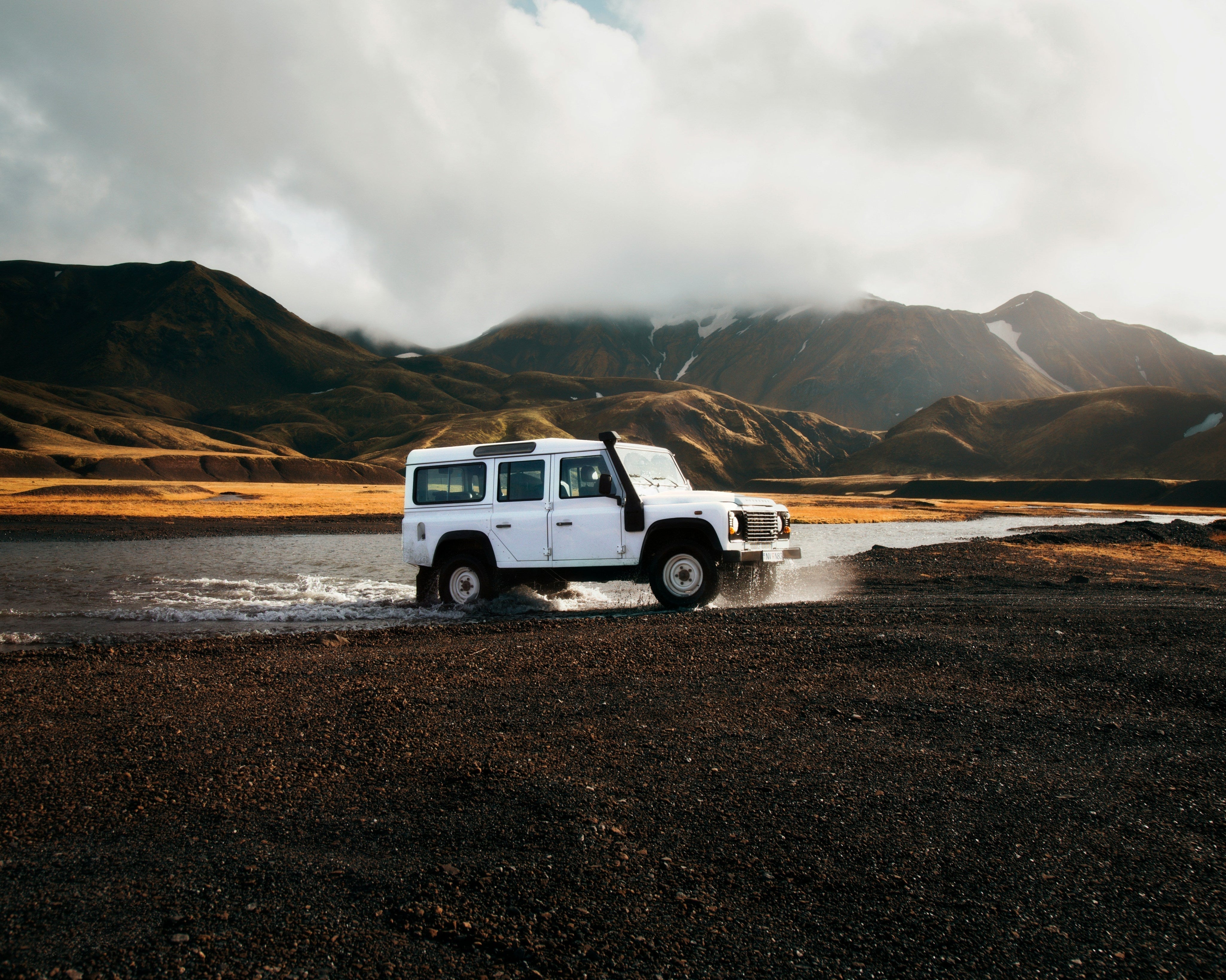 Vit terrängbil kör genom ett grunt vattendrag med berg i bakgrunden – symbol för beredskap och krisförmåga vid resor i naturen.