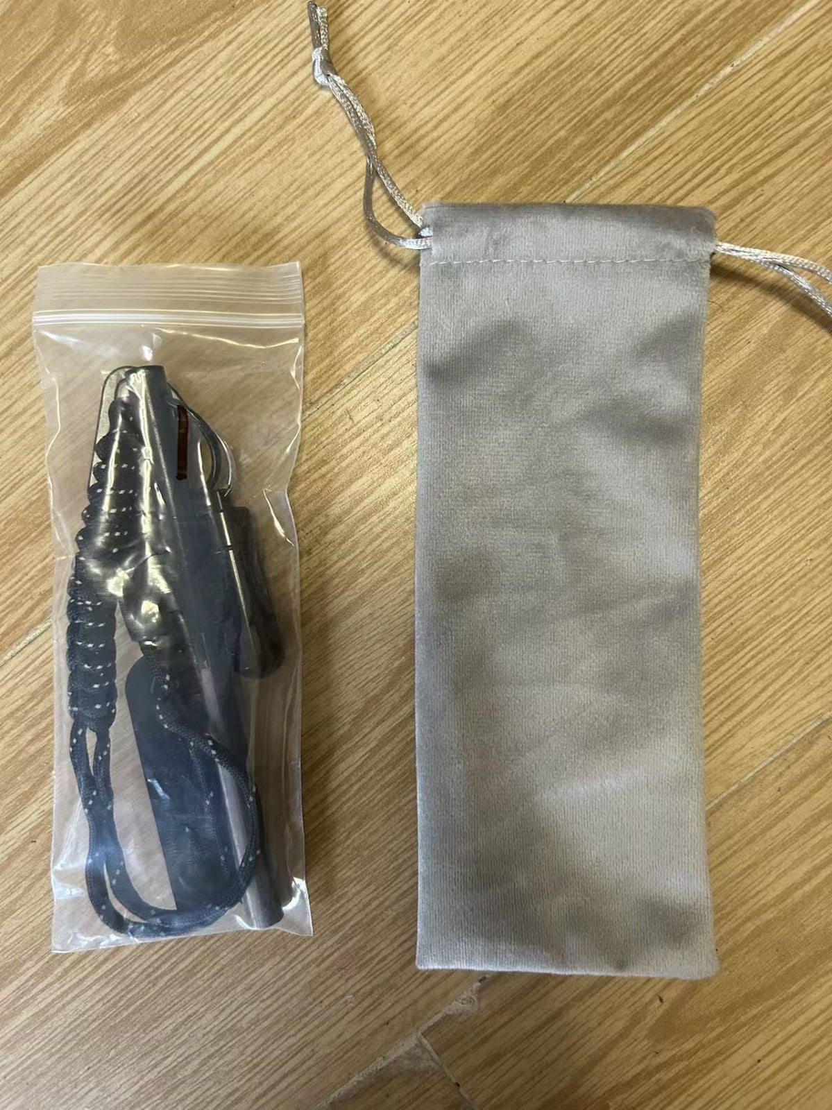 En plastförpackning med en svart visselpipa och en grå tygpåse ligger på ett trägolv.
