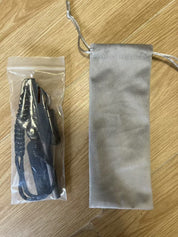 En plastförpackning med en svart visselpipa och en grå tygpåse ligger på ett trägolv.