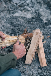 En person täljer i en träbit med en kniv för att förbereda ved för en eld.