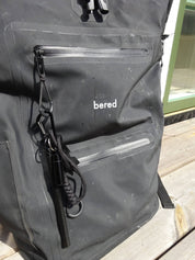 En svart, vattentät ryggsäck med "bered" logotyp, har en tändstål fäst vid en dragkedja.